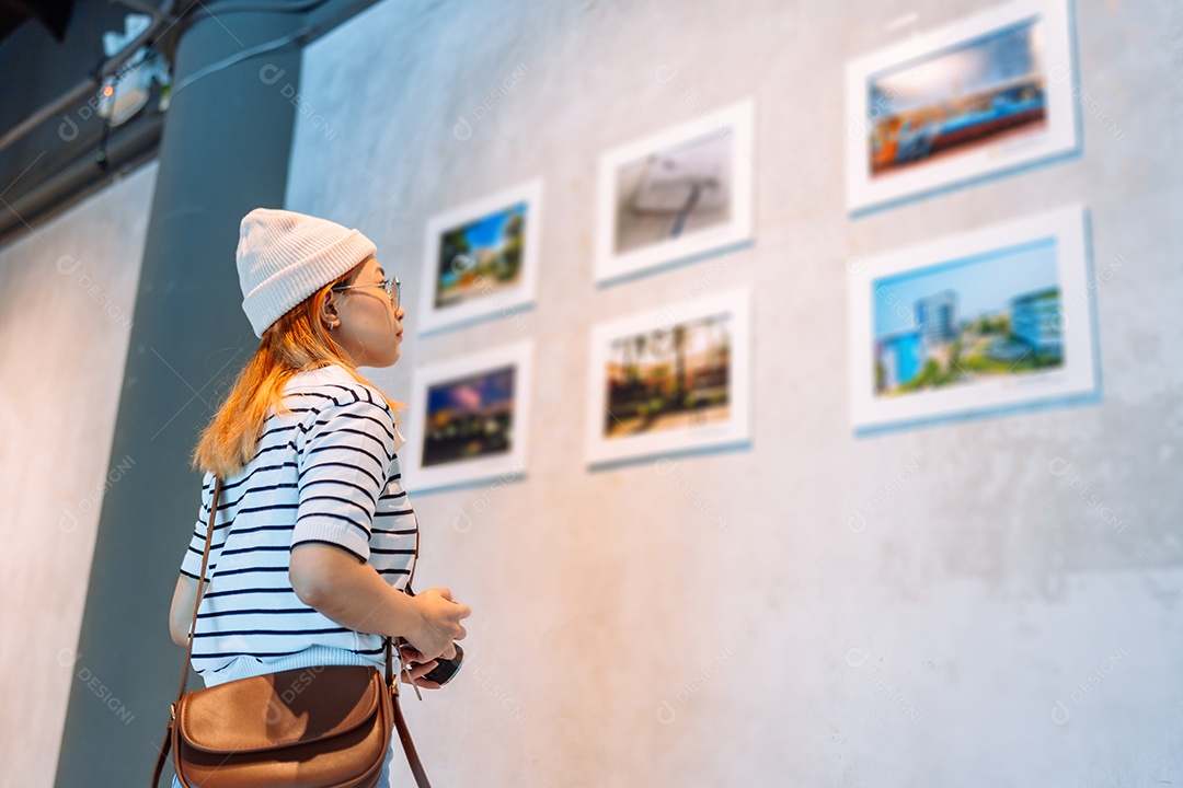 Mulher visitando a galeria de arte suas fotos olhando na parede, observando quadro