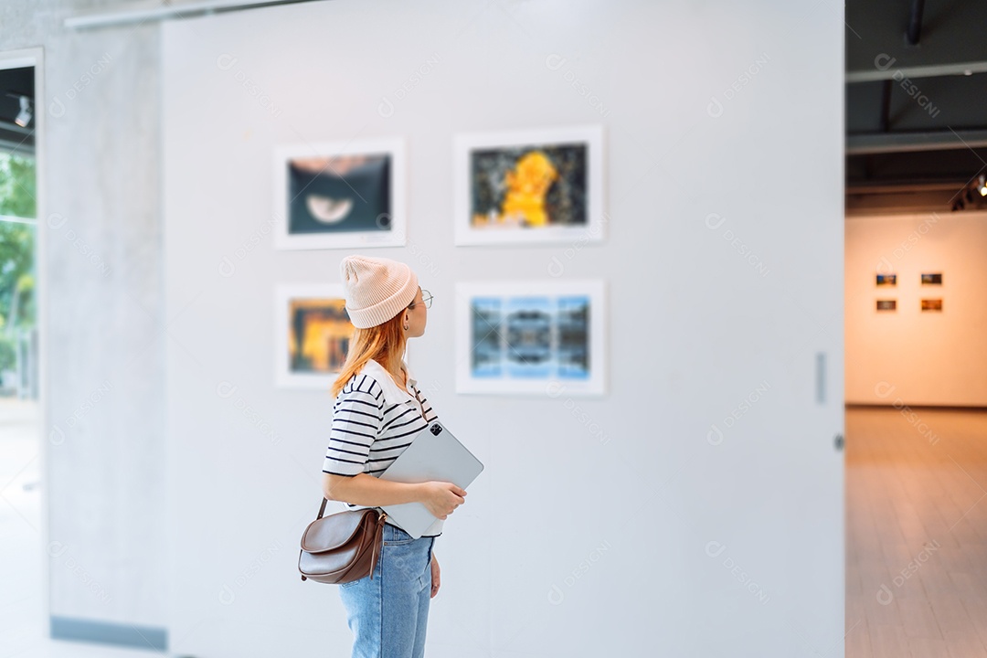 Mulher visitando a galeria de arte suas fotos olhando na parede, observando quadro