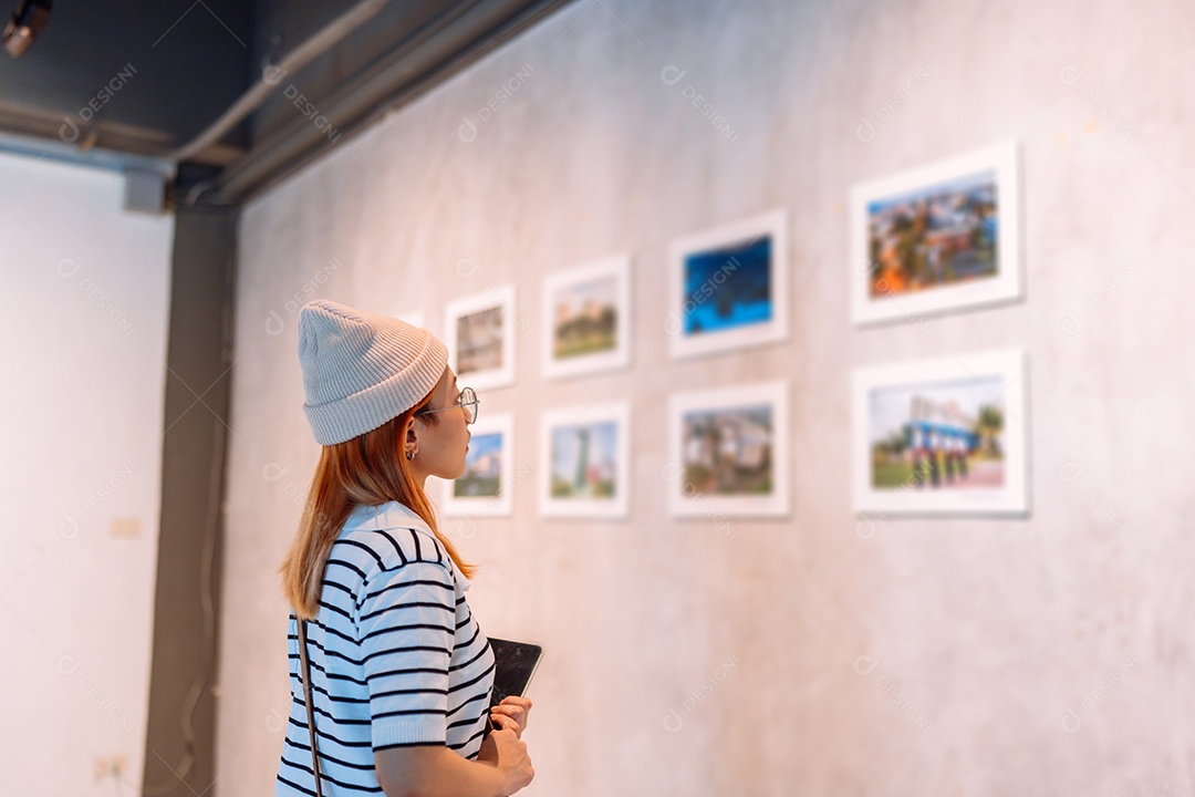 Mulher visitando a galeria de arte suas fotos olhando na parede, observando quadro