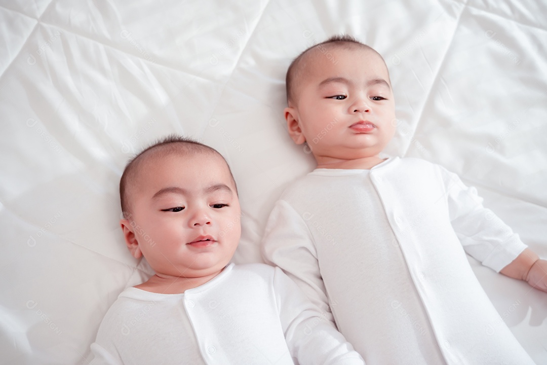 Bebês gêmeos recém-nascidos deitados em uma cama branca em casa.