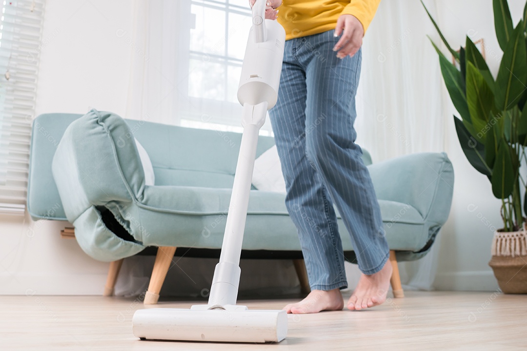 Mulher asiática feliz usando aspirador de pó enquanto limpa o chão em casa