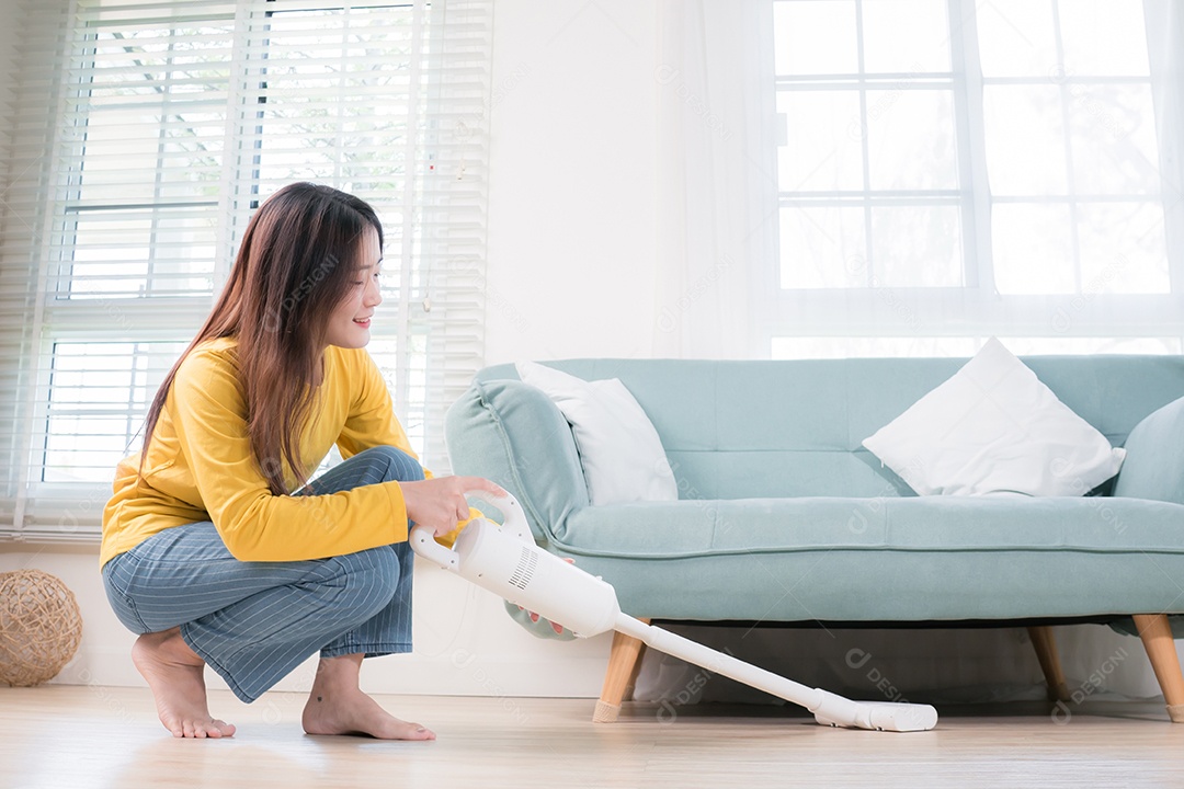 Mulher asiática feliz usando aspirador de pó enquanto limpa o chão em casa