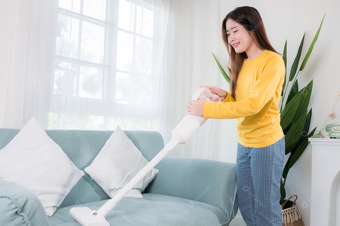 Mulher asiática feliz usando aspirador de pó enquanto limpa o chão em casa