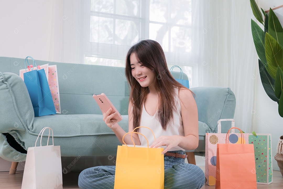 Mulher asiática sorridente sentada no sofá com sacolas de compras