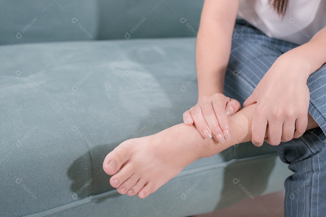 Mulher asiática ela tem dor no pé no sofá na sala de estar em casa