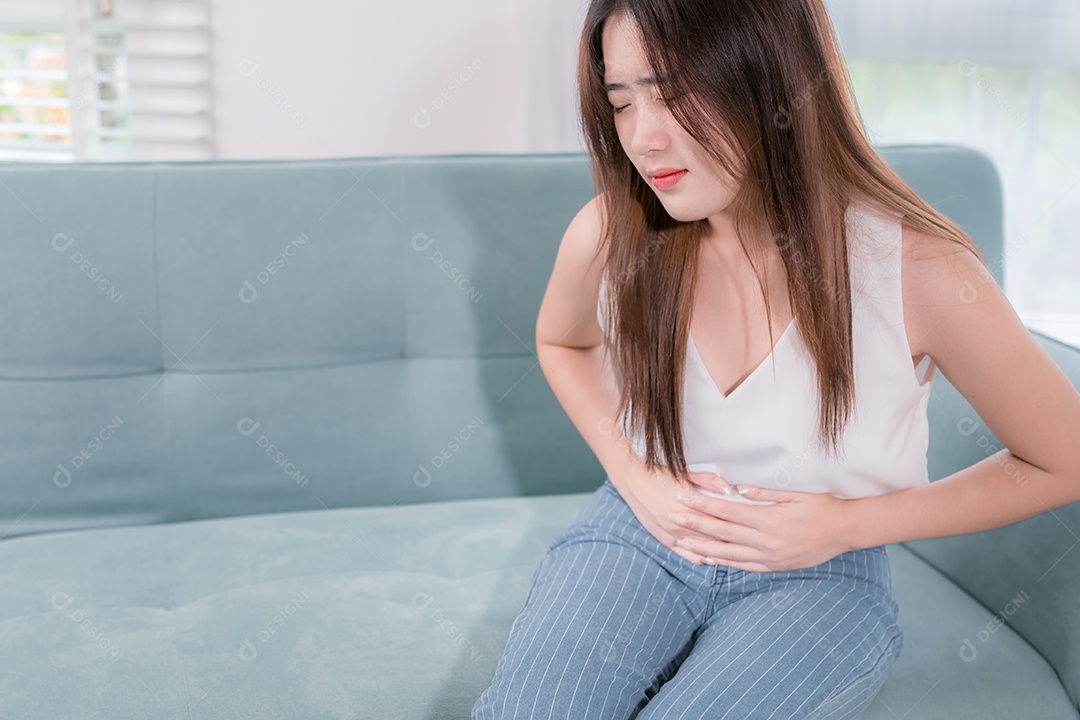 Mulher asiática com dor de estômago sentada no sofá na sala de estar