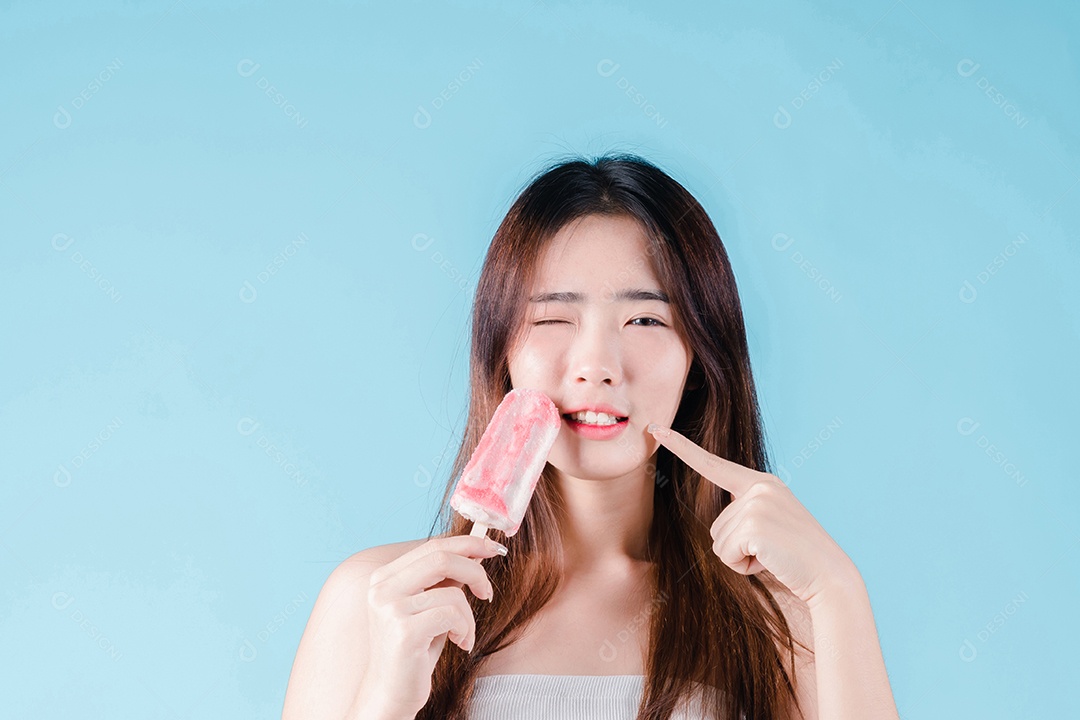 Mulher asiática segura picolé tem dentes hipersensíveis no fundo azul