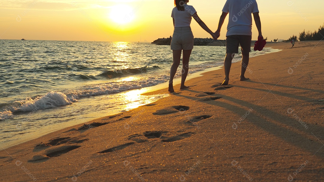 Casal de mãos dadas andando na areia da praia