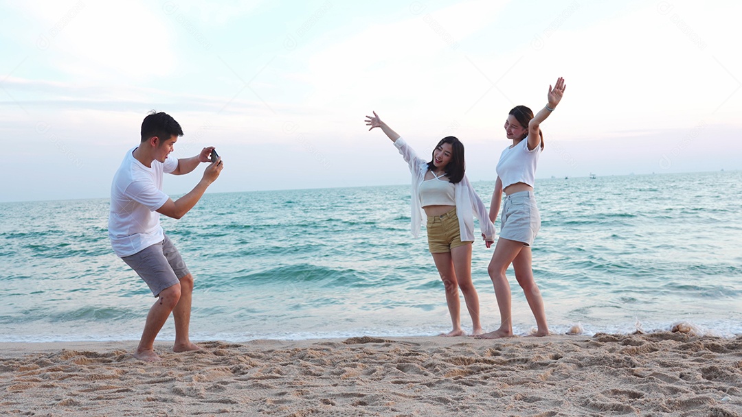 Jovem segurando câmera tirando foto de adolescentes posando na praia no verão