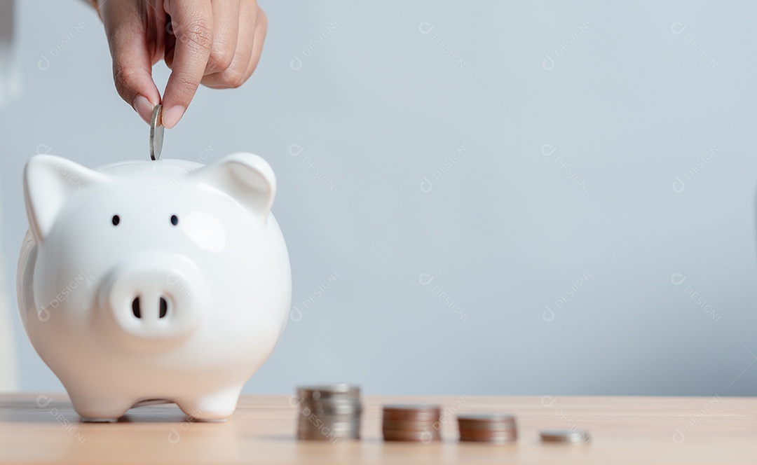 Mão de mulher colocando algumas moedas dentro de um cofre de porquinho de cerâmica