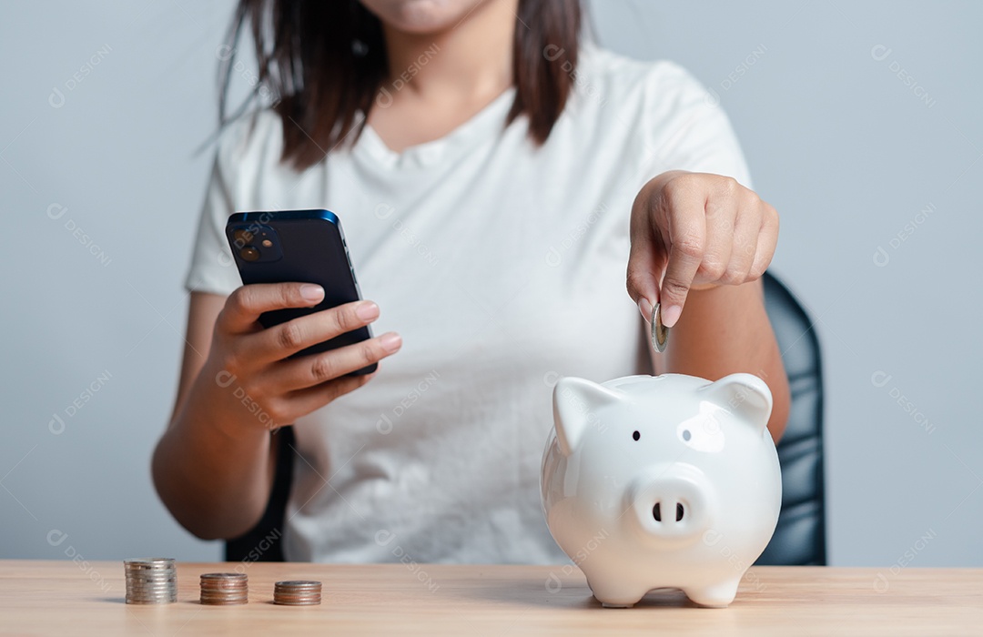 Mão de mulher colocando algumas moedas dentro de um cofre de porquinho de cerâmica