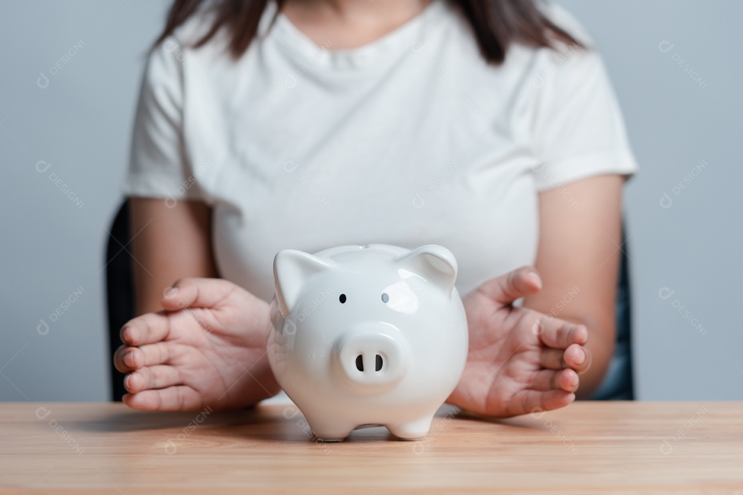 Mão de mulher segurando cofre de porquinho sobre a mesa