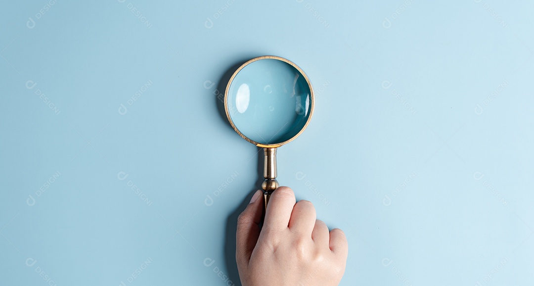 Mãos de mulher segurando lupa em fundo azul