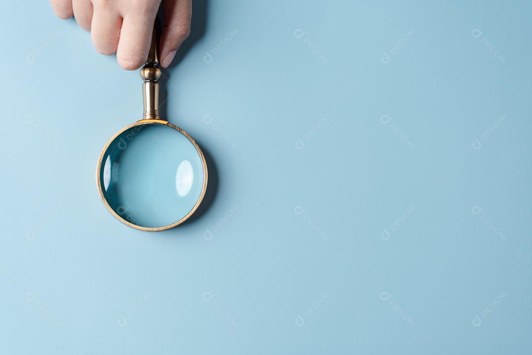 Mãos de mulher segurando lupa em fundo azul