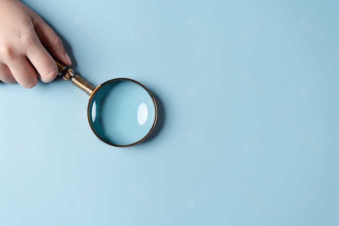 Mãos de mulher segurando lupa em fundo azul