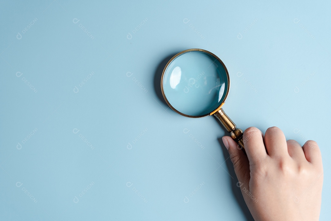 Mãos de mulher segurando lupa em fundo azul