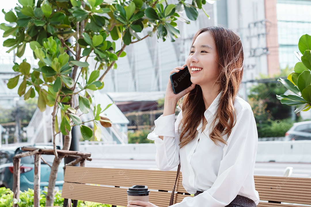 Linda mulher asiática usando celular sentada no banco da praça