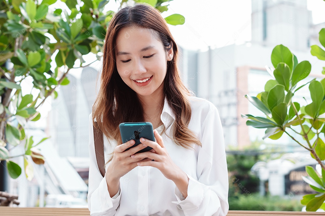 Linda mulher asiática usando celular sentada no banco da praça