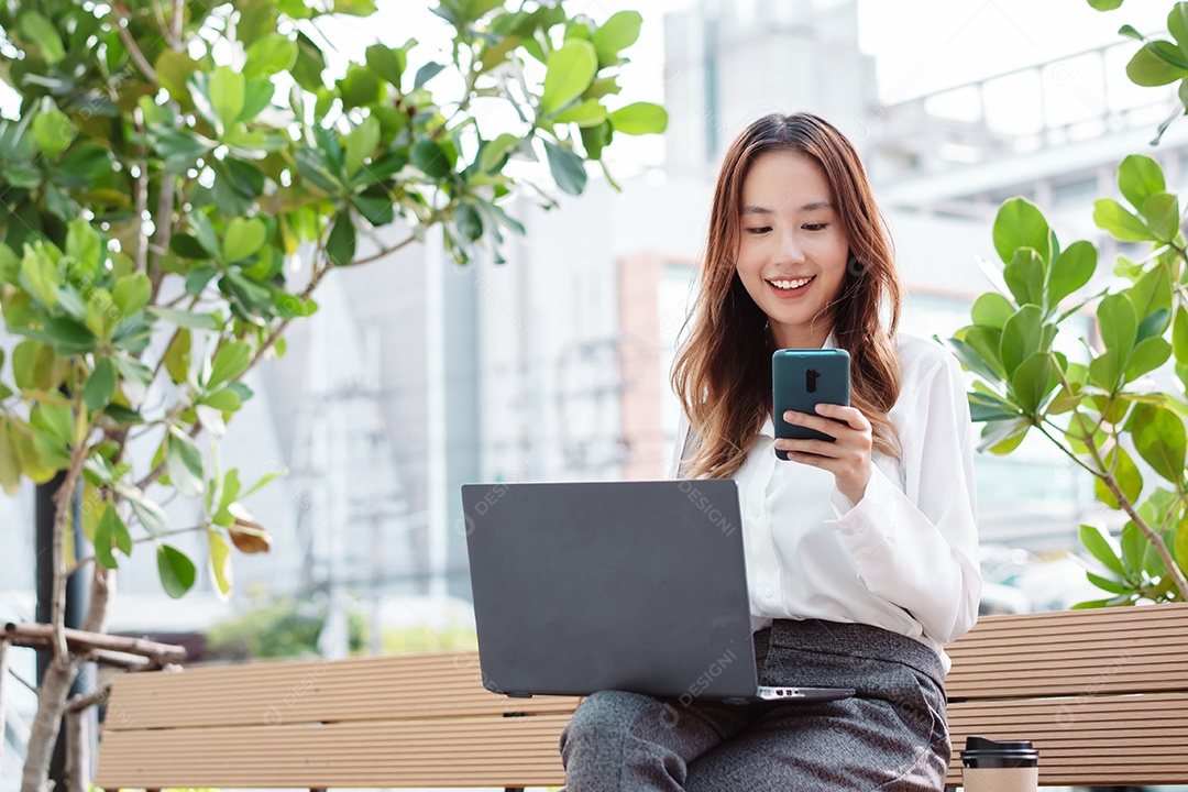 Linda mulher asiática usando notebook sentada no banco da praça