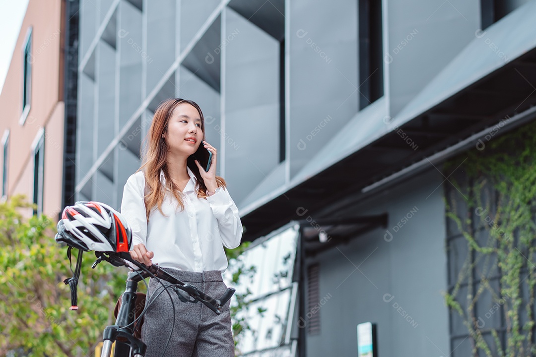 Linda mulher asiática sorridente com bicicleta falando ao celular