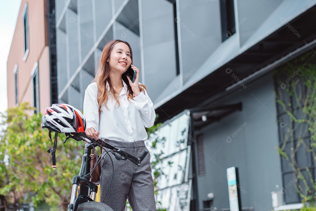 Linda mulher asiática sorridente com bicicleta falando ao celular
