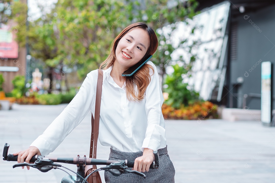 Linda mulher asiática sorridente com bicicleta falando ao celular