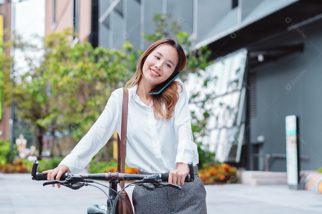Linda mulher asiática sorridente com bicicleta falando ao celular