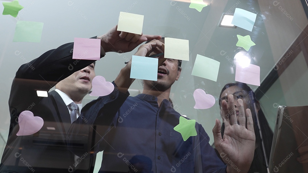 Homem de negócios jovem com brainstorming de trabalho em equipe usando post-its para compartilhar ideias na parede de vidro