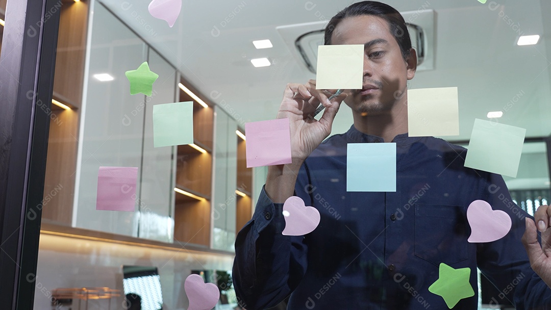 Homem de negócios jovem com brainstorming de trabalho em equipe usando post-its para compartilhar ideias na parede de vidro