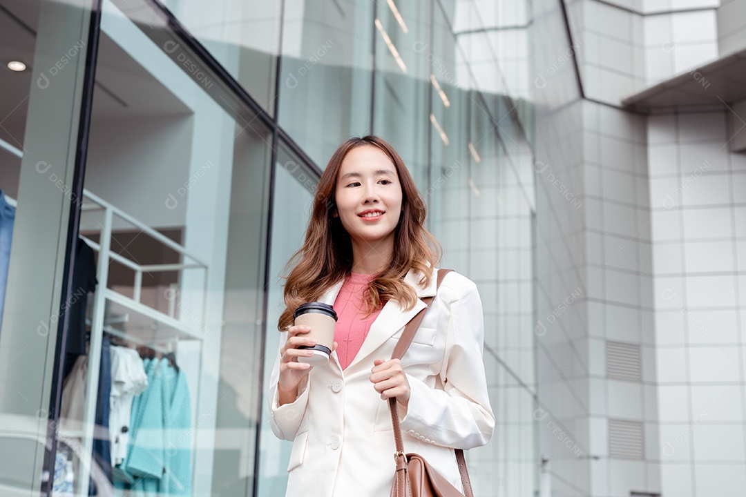 Linda empresária asiática usa smartphone segurando copo de papel com bebida quente