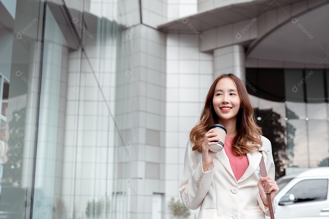 Linda empresária asiática usa smartphone segurando copo de papel com bebida quente