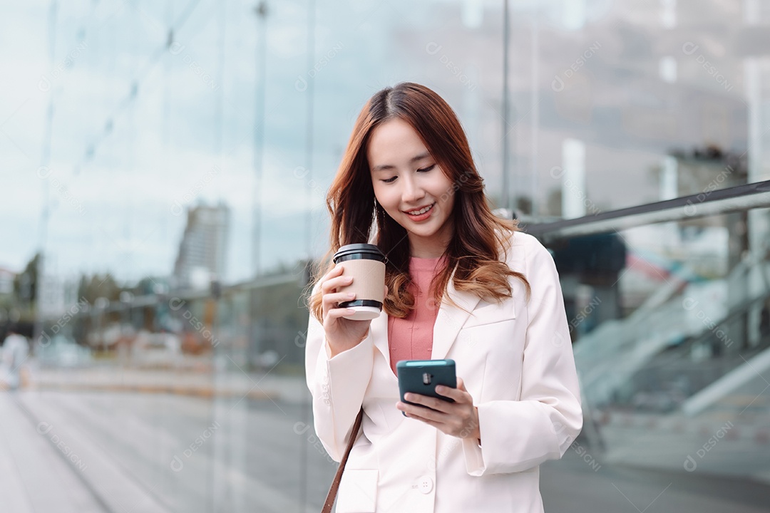 Linda empresária asiática usa smartphone segurando copo de papel com bebida quente