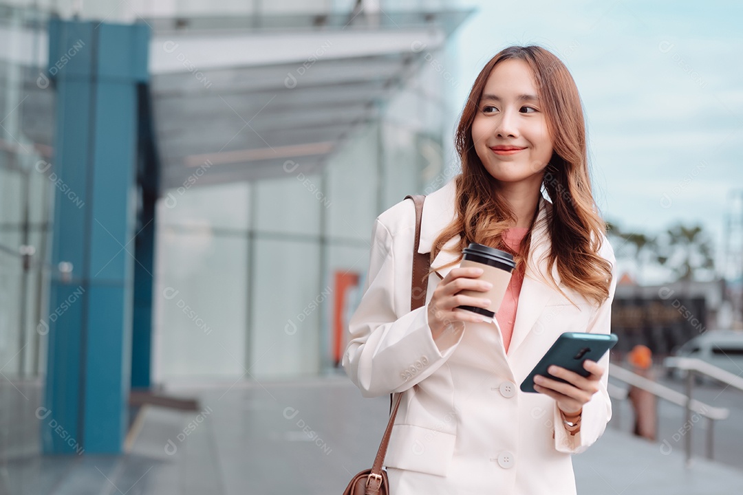 Linda empresária asiática usa smartphone segurando copo de papel com bebida quente