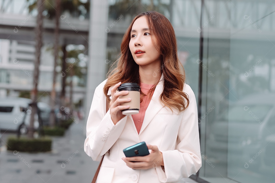 Linda empresária asiática usa smartphone segurando copo de papel com bebida quente