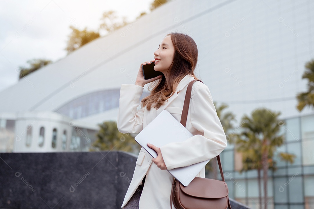 Linda empresária asiática usa smartphone e segura laptop