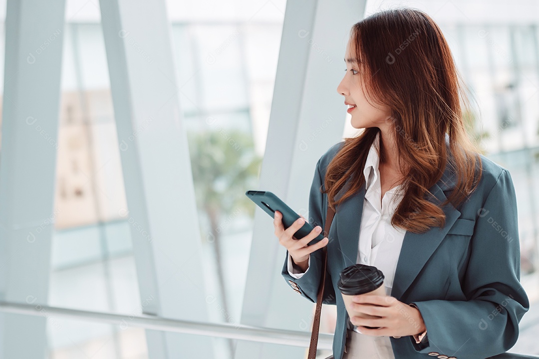 Linda empresária asiática usa smartphone segurando um copo de papel com bebida quente