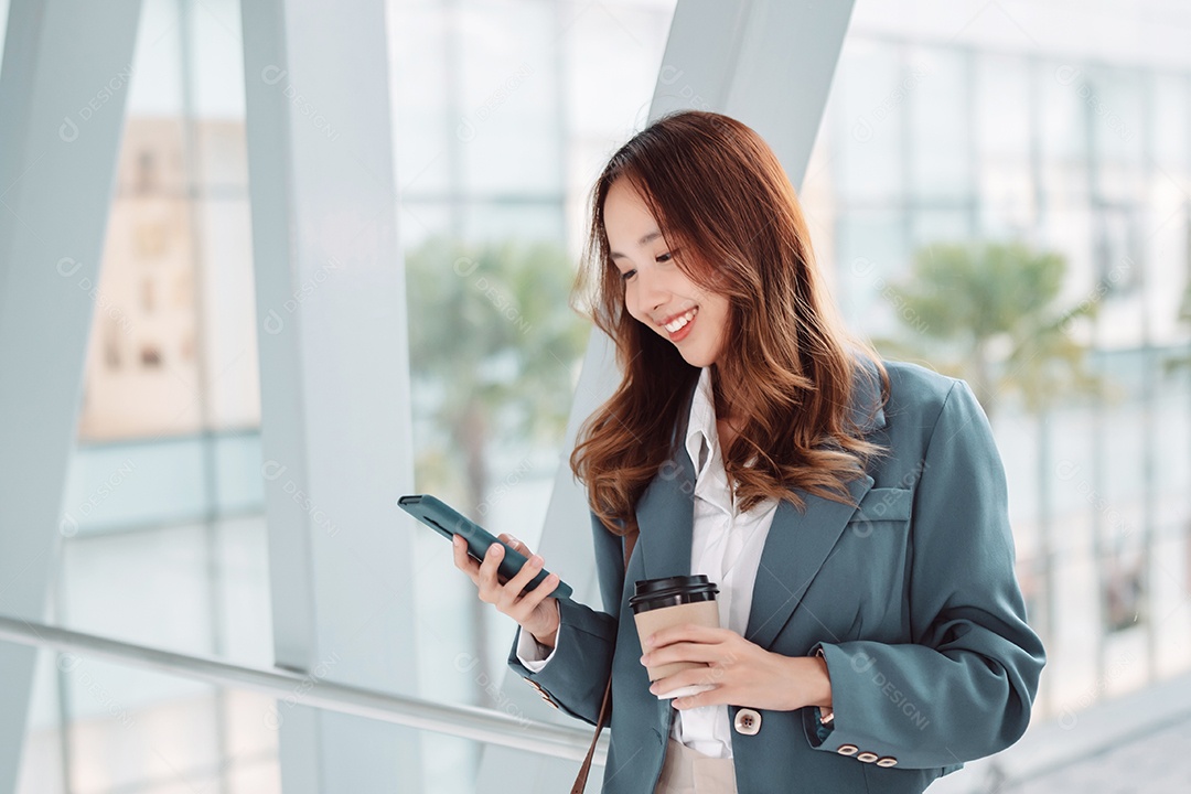 Linda empresária asiática usa smartphone segurando um copo de papel com bebida quente