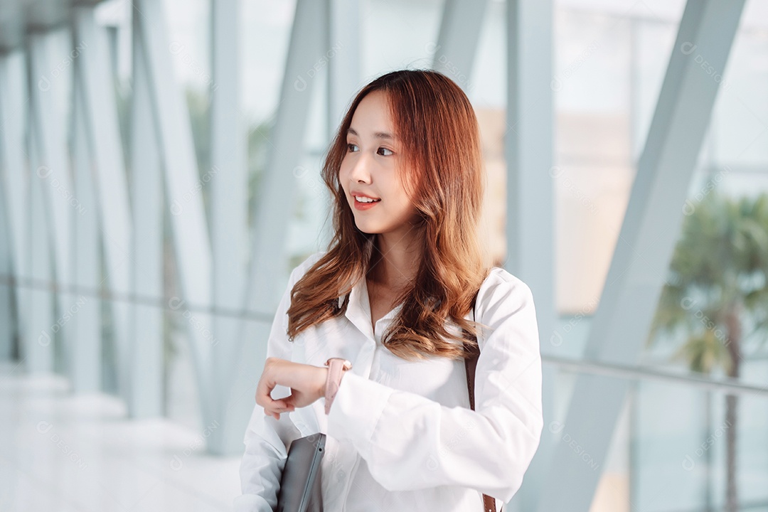 A empresária asiática sorridente segura o computador portátil enquanto se desloca