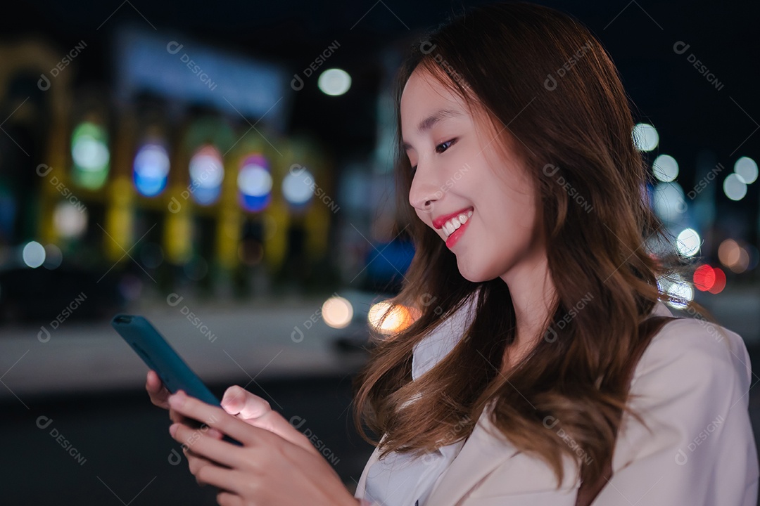 Encantadora empresária asiática usa telefone celular na cidade à noite