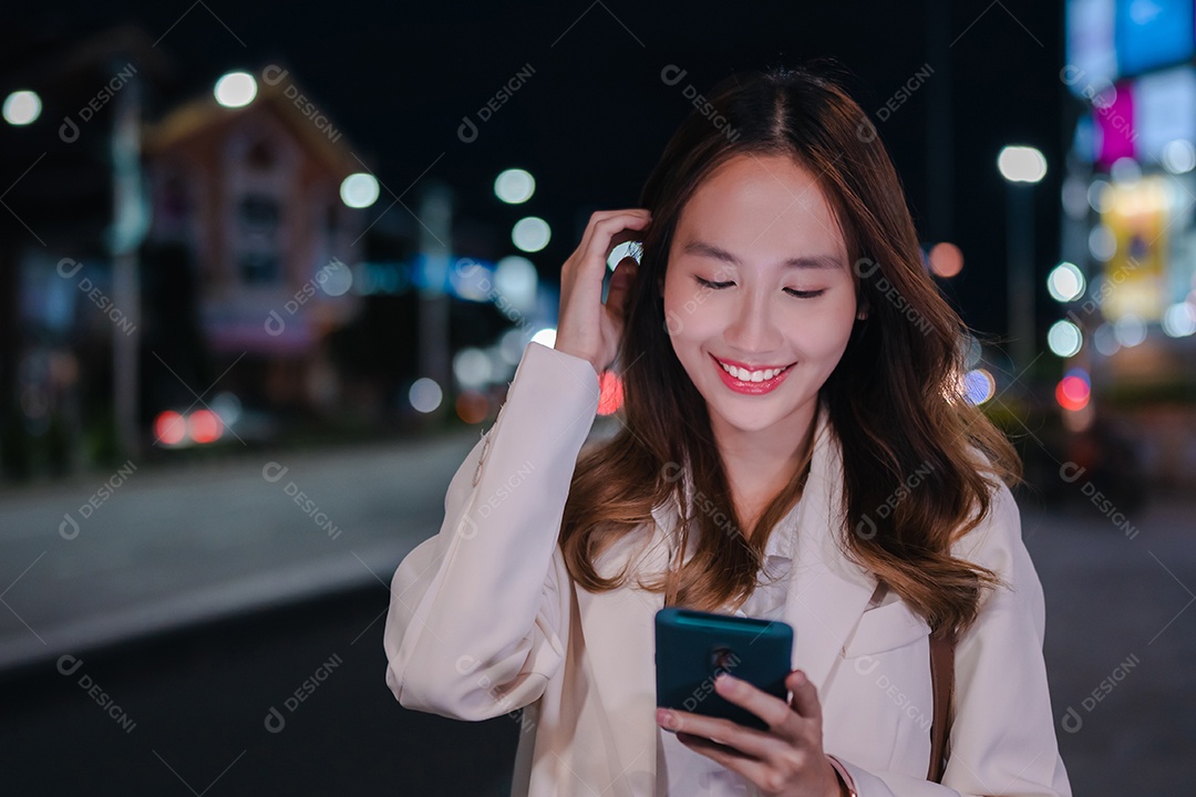Encantadora empresária asiática usa telefone celular na cidade à noite