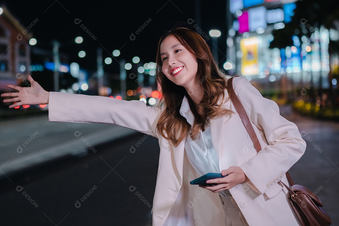 Empresária asiática usa telefone celular para chamar táxi em aplicativo na rua da cidade à noite