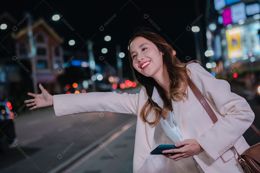 Empresária asiática usa telefone celular para chamar táxi em aplicativo na rua da cidade à noite