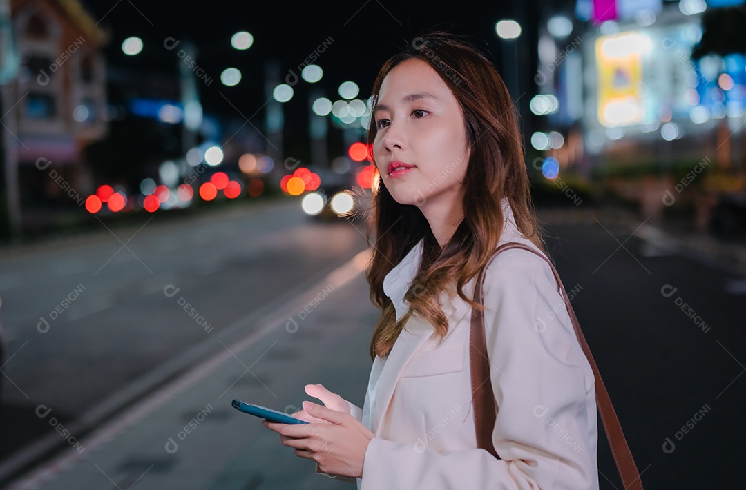 Empresária asiática usa telefone celular para chamar táxi em aplicativo na rua da cidade à noite
