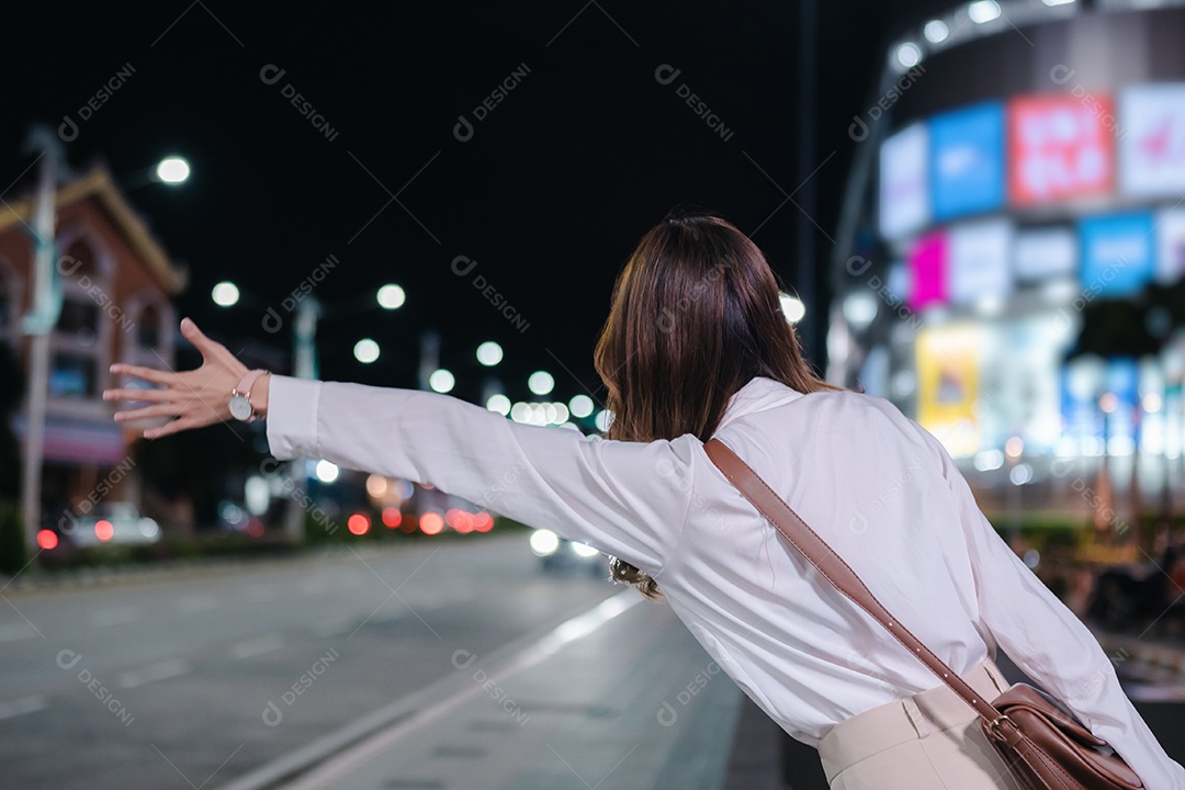 Empresária asiática usa telefone celular para chamar táxi em aplicativo na rua da cidade à noite