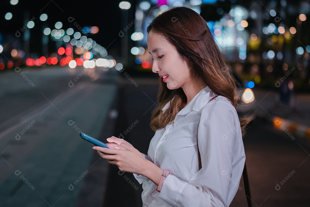 Empresária asiática usa telefone celular para chamar táxi em aplicativo na rua da cidade à noite