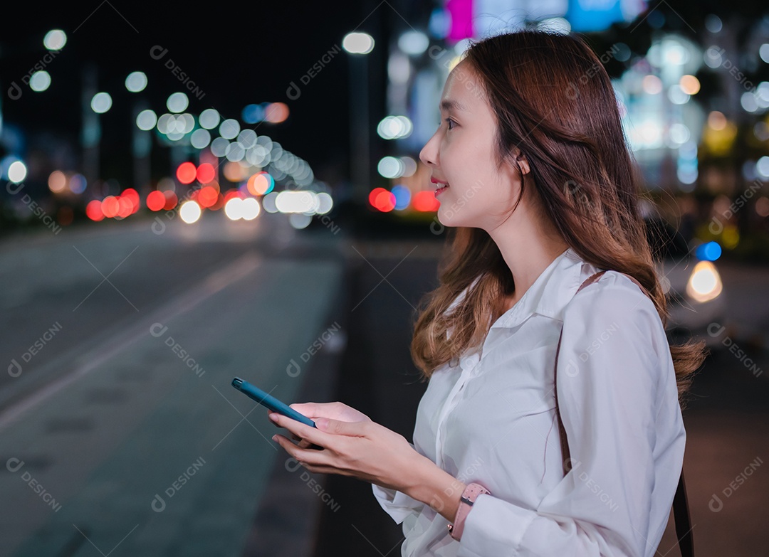 Empresária asiática usa telefone celular para chamar táxi em aplicativo na rua da cidade à noite