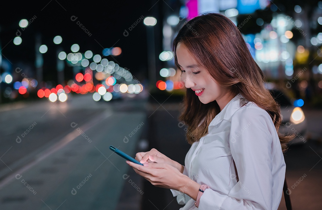 Encantadora empresária asiática usa telefone celular na cidade à noite