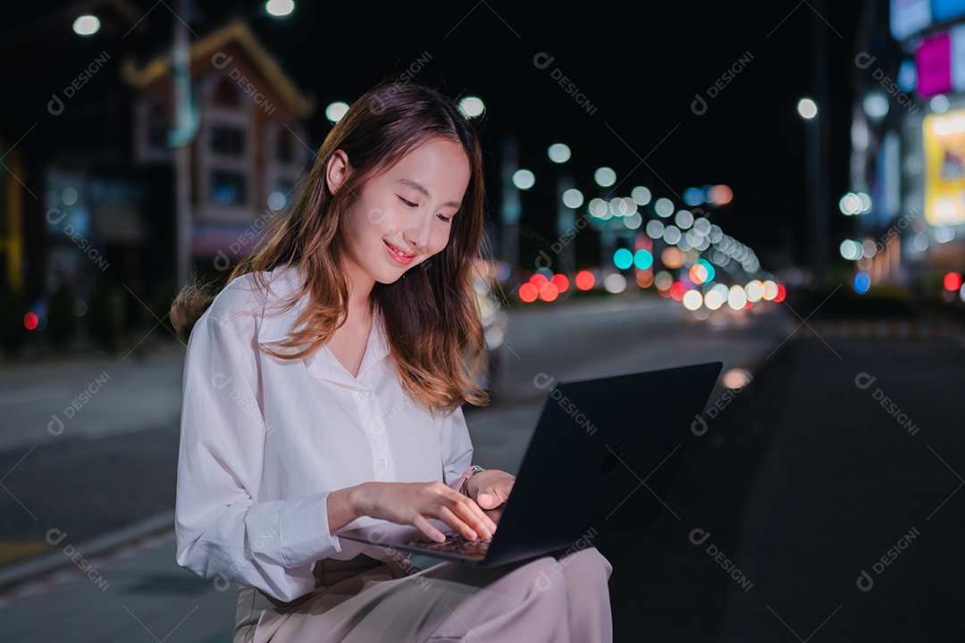 Encantadora empresária asiática usa laptop na cidade à noite