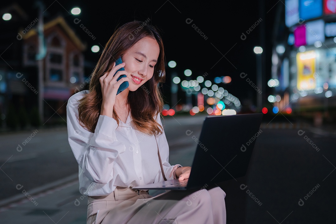 Encantadora empresária asiática usa laptop na cidade à noite