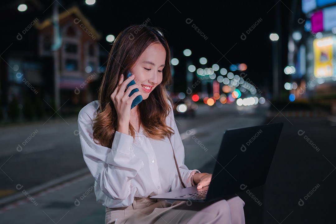 Encantadora empresária asiática usa laptop na cidade à noite